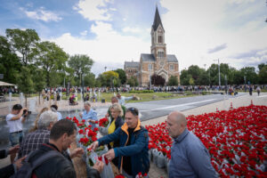 A Palota Parkban veszik át a muskátlikat a lakosok, háttérben a Széchenyi téri templom ékeskedik.